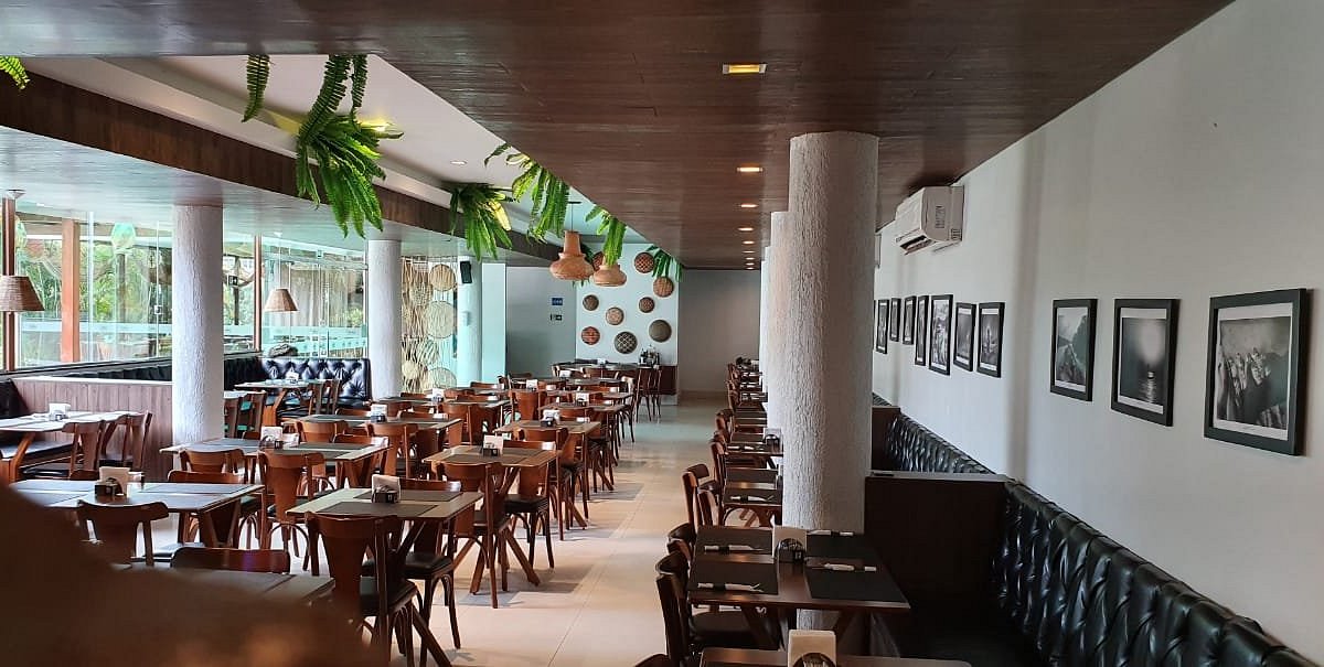 Salão climatizado do Restaurante Palhoça com mesas de madeira, folhagens e fotografias nas paredes