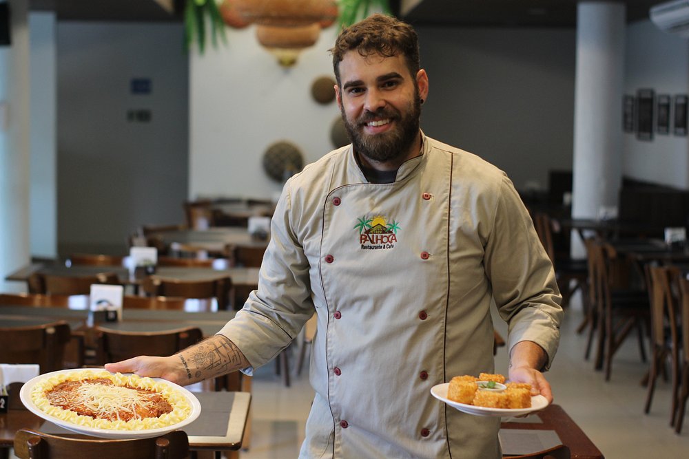 Chef do Restaurante Palhoça segurando dois pratos no salão