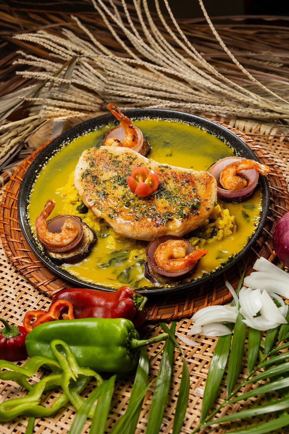 Prato com molho amarelo, camarões, cebola roxa, folhas e cestaria